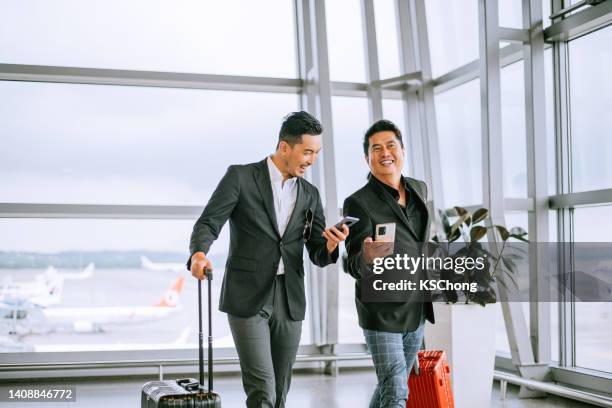 two businessmen pulling suitcase in modern airport terminal - business man walking with a bag in asia stockfoto's en -beelden