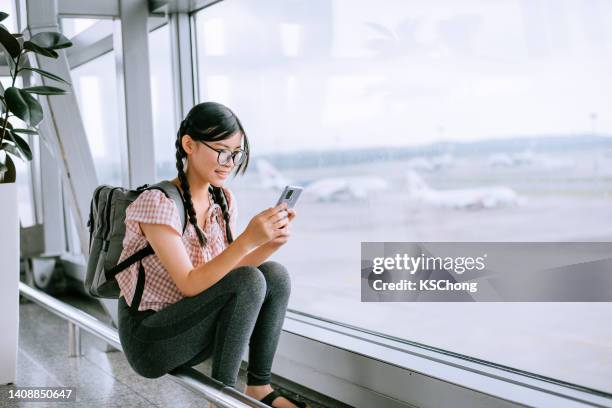 tween girl looking at smartphone at airport - asian girl in leggings stock pictures, royalty-free photos & images