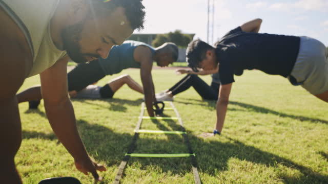 Group of fit and diverse sports people doing training circuit exercises with weights on sports field outside. Dedicated athletes practising workout drills to gain and strengthen muscles and endurance