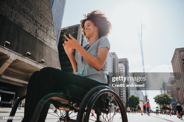 mujer en silla de ruedas en la calle usando un teléfono inteligente - accesibilidad fotografías e imágenes de stock