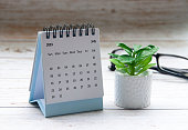 July 2023 white desk calendar on wooden table with plant and glasses background.