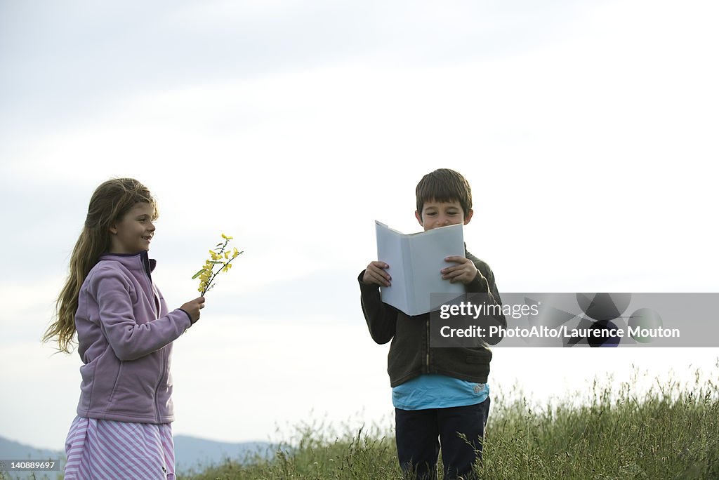 Children in field, boy reading book while girl picks wildflowers