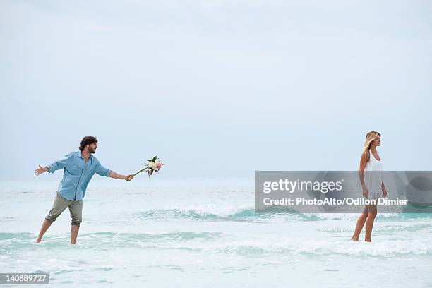 couple standing in sea, woman walking away from man as he holds out a bouquet - man holding out flowers stock pictures, royalty-free photos & images