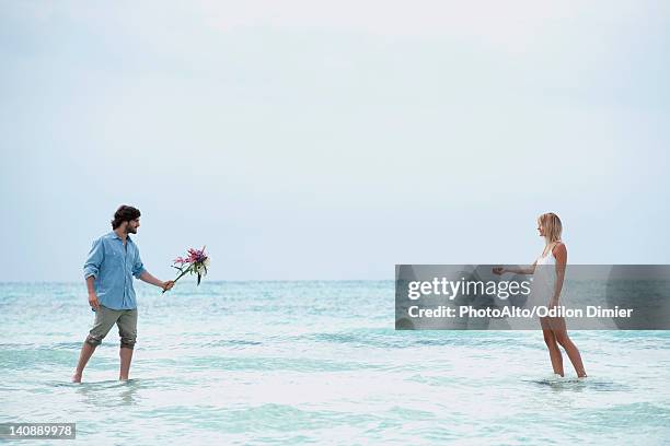 couple walking in sea towards each other, man holding out bouquet - man holding out flowers stock pictures, royalty-free photos & images