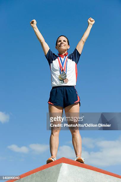 female athlete standing on winner's podium with arms raised in victory - sportsperson medal stock pictures, royalty-free photos & images