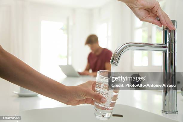woman filling glass of water at kitchen sink, cropped - wasser ressource stock-fotos und bilder
