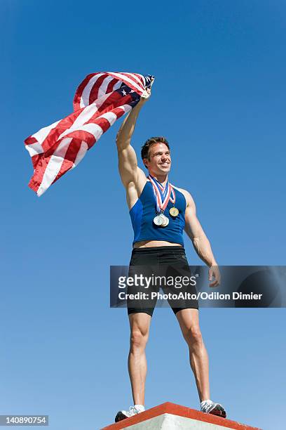 male athlete on winner's podium, holding up american flag - olympic podium stock pictures, royalty-free photos & images