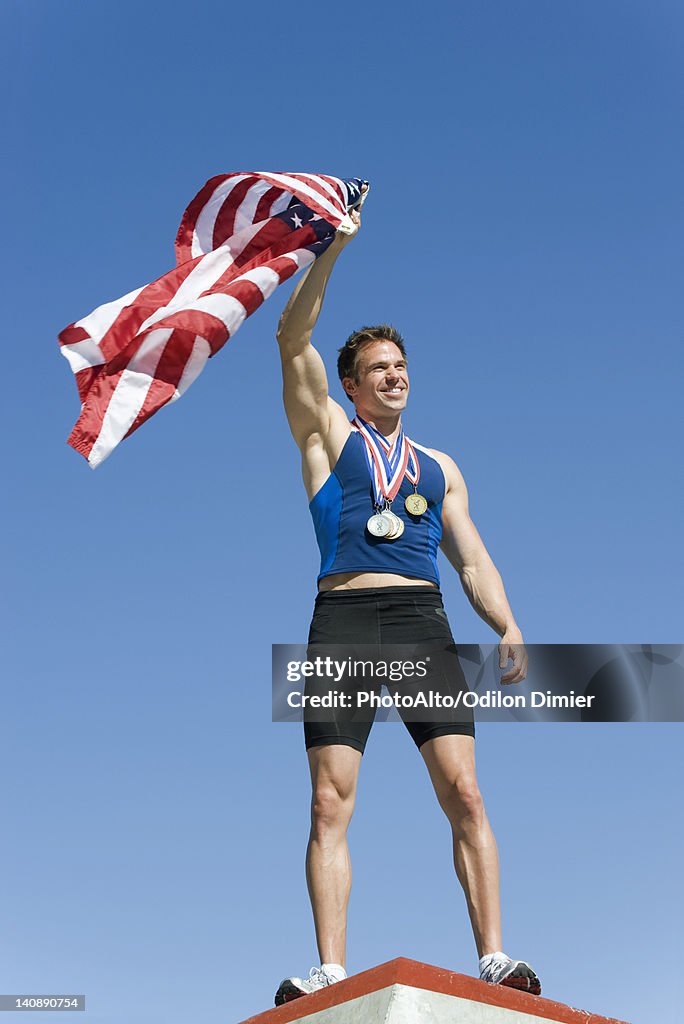 Male athlete on winner's podium, holding up American flag