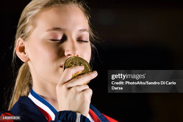 female athlete kissing gold medal, portrait - teen awards stock-fotos und bilder