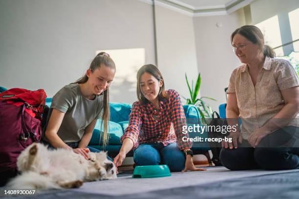 host-mother welcoming and explaining how to take care of dog to two multi-ethnic female tourists - dog greeting stock pictures, royalty-free photos & images