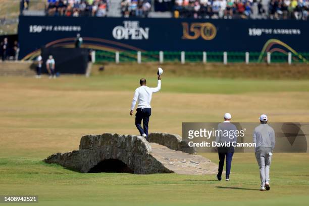 Tiger Woods of The United States waves to the crowds as he walks over the Swilcan Bridge on the 18th hole as his playing partners Max Homa and...