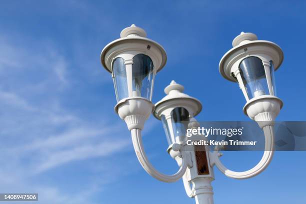 the top of a white, three light post lamp in a blue sky with sparse clouds - street light post stock pictures, royalty-free photos & images
