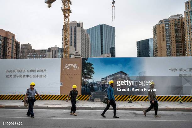 Construction workers walk by signs advertising a development project being built as they leave following their shift on July 15, 2022 in Beijing,...