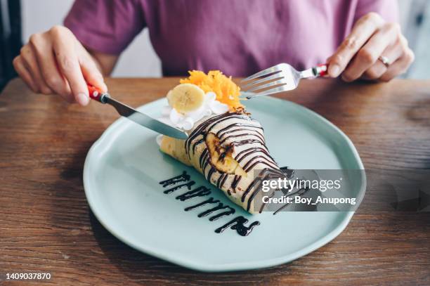cropped shot of woman trying to eat a banana cold crepe cake with fork and knife. - nutella pancake stock pictures, royalty-free photos & images