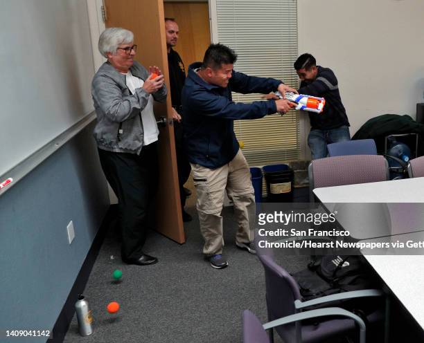 Marsha Jaeger, left, and Juan Manriquez, right, role play defending themselves against "shooter" Boun Khannoume, center, during an active shooter...