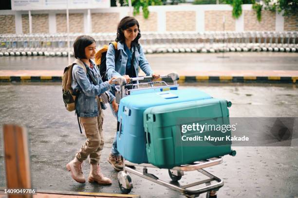 mother and daughter carrying luggage on a luggage cart at airport - luggage trolley stockfoto's en -beelden