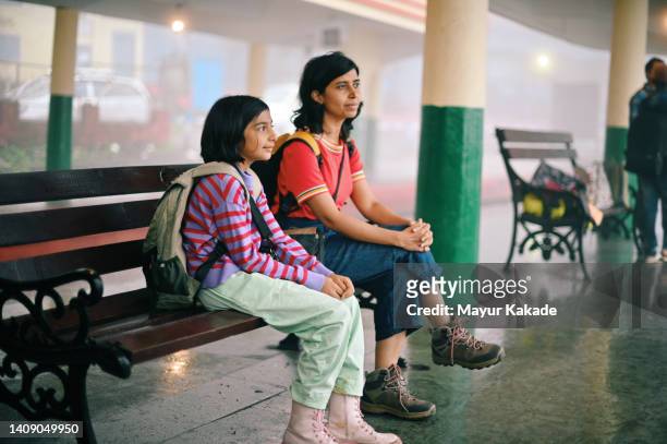 mother and daughter waiting at a train station platform, sitting on a bench - bengali girl stock-fotos und bilder