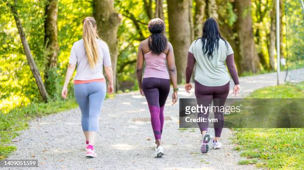 three women in sportswear walking in public park, back view - power walking stock pictures, royalty-free photos & images