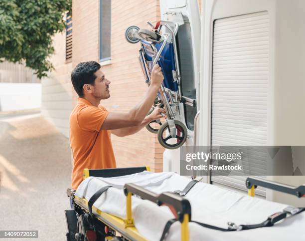 portrait of a paramedic taking a wheelchair out of an ambulanceparamedic is young and wears orange - stretcher stock-fotos und bilder