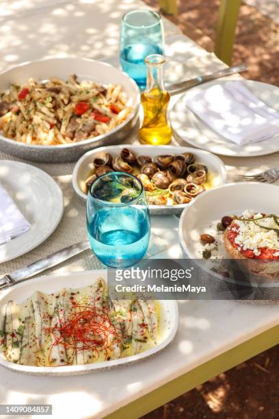 griechischer esstisch mit essen und tellern unter olivenbäumen mit kretischen köstlichkeiten - greek food stock-fotos und bilder