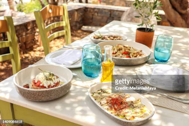 greek dinner table with food and plates under olive trees with cretan delicacies - cheesy fries stock pictures, royalty-free photos & images