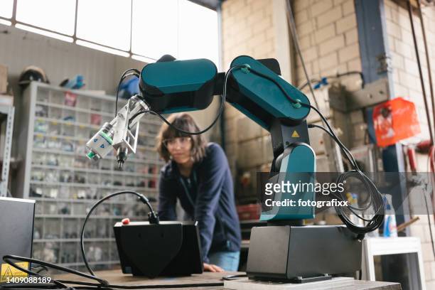 female technician programs a robot arm with a digital tablet - robotics stockfoto's en -beelden