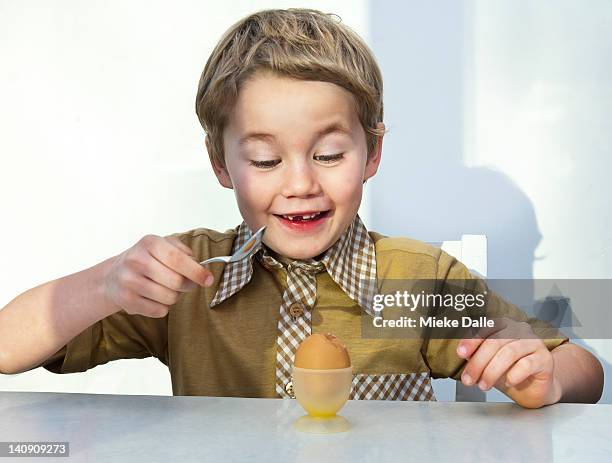 boy cracking a boiled egg with a spoon - kid boiled egg stock pictures, royalty-free photos & images