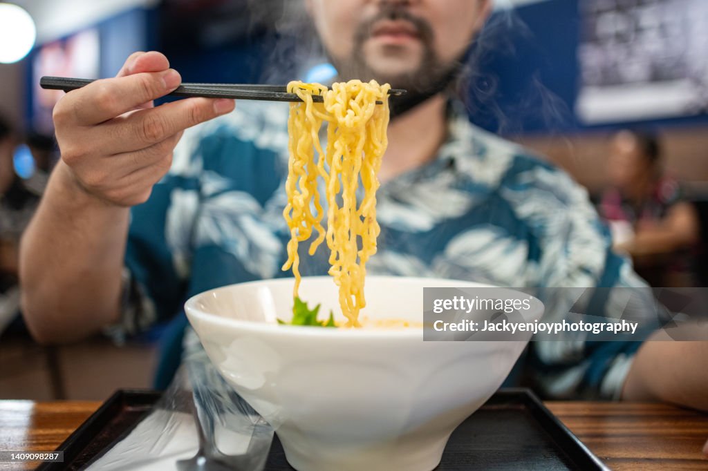 Close-up of man eating ramen soup with noodles, pork and egg