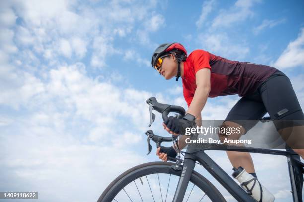 asian female cyclist riding a bicycle against the sky. - biker photos et images de collection