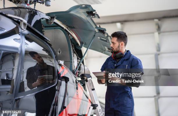 male aero engineer with clipboard checking on helicopter in hangar - helicopter pilot stock pictures, royalty-free photos & images
