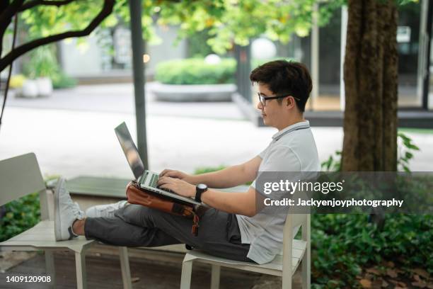 young asian entrepreneur working at his laptop while drinking coffee in an urban office park. - ambassadors residence stock pictures, royalty-free photos & images