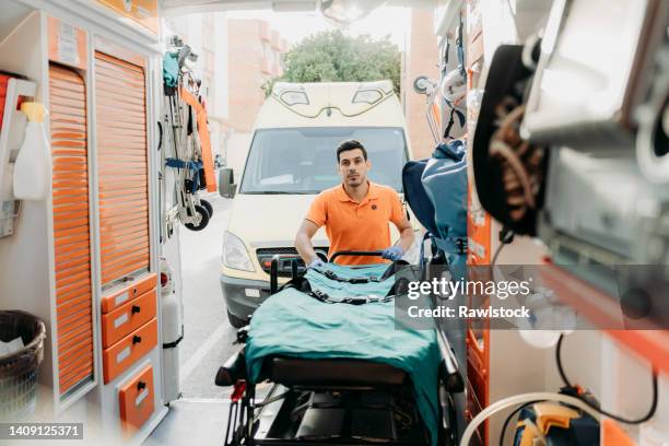 photo of a paramedic through the ambulance as he works pulling out the stretcher - stretcher stock-fotos und bilder