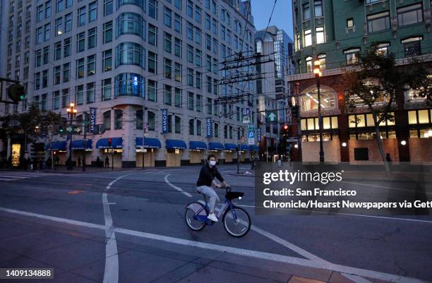 Bicyclist rides along an empty Market Street toward as police officers from multiple agencies keep an eye on downtown when curfew takes hold in San...