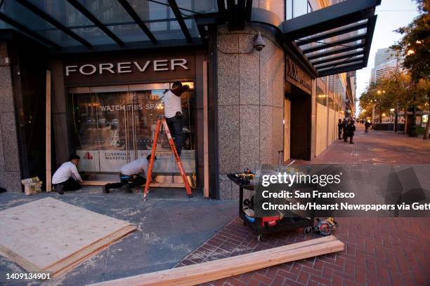 Workers finish boarding up a storefront on Market Street as police officers from multiple agencies keep an eye on downtown as curfew takes hold in...