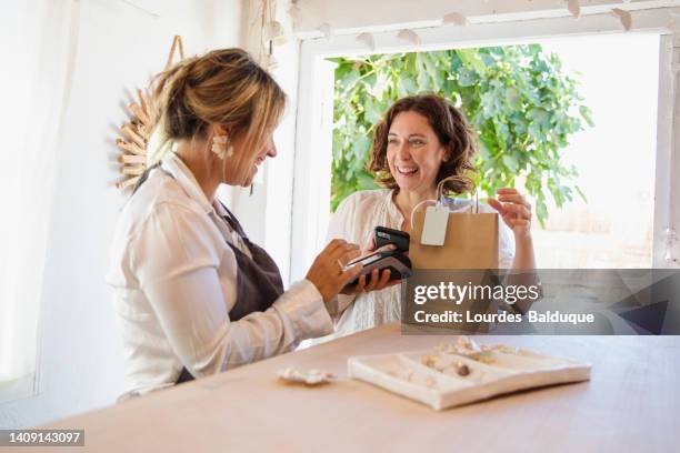 happy woman paying with her phone in small business - mobile payment stock pictures, royalty-free photos & images