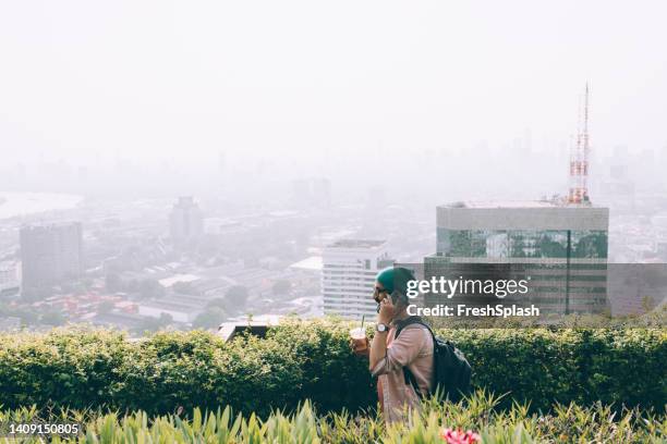 a side view of a smiling casually dressed influencer with a backpack  talking on his mobile phone while walking through the city park - walking side view bildbanksfoton och bilder