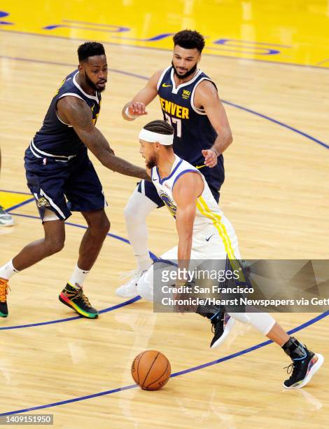 Stephen Curry dribbles by JaMychal Green and Jamal Murray during the first half as the Golden State Warriors played the Denver Nuggets in their first...