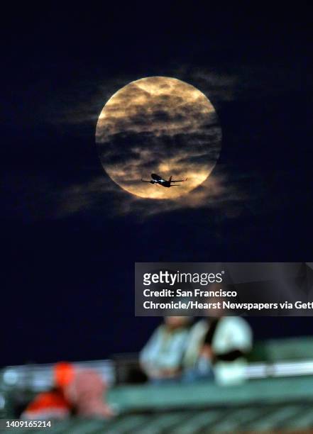 Plane flies in front of the Pink Super Moon as it rises behind fans on the Levi's Landing wall as the San Francisco Giants played the Colorado...