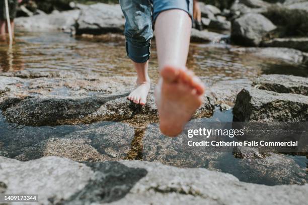 a barefoot child takes a step towards the camera, over rocks and water - naderen stockfoto's en -beelden