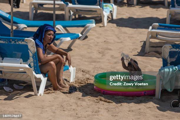 Woman on the beach in the sun while her daughter has fun in the water pool as a heatwave sweeps across Spain on July 16, 2022 in Benidorm, Spain.