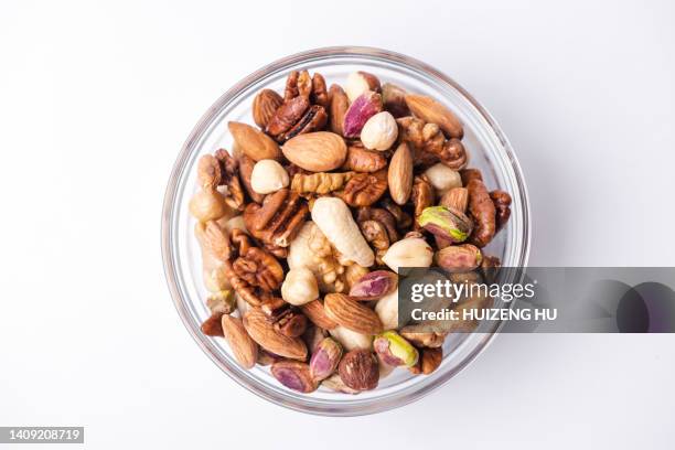 mixed nuts in a glass bowl on white background. nuts mix pistachios, almonds, walnuts, hazelnuts, cashews - pijnboompit stockfoto's en -beelden