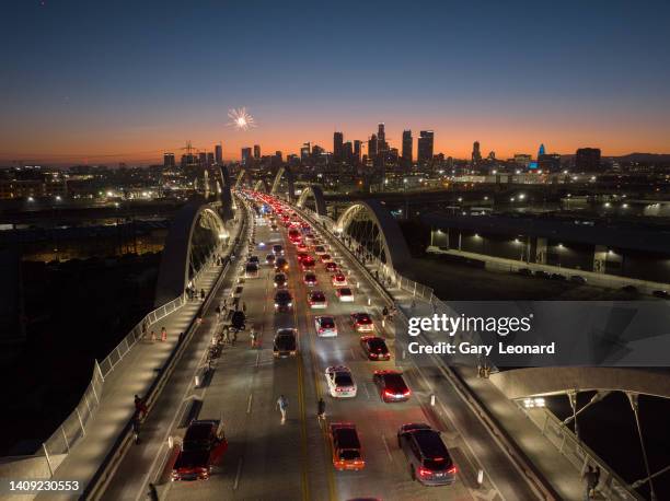 At night a drone view of fireworks over the downtown skyline as the bridge is filled with cruising cars as part of a low-rider event during the...