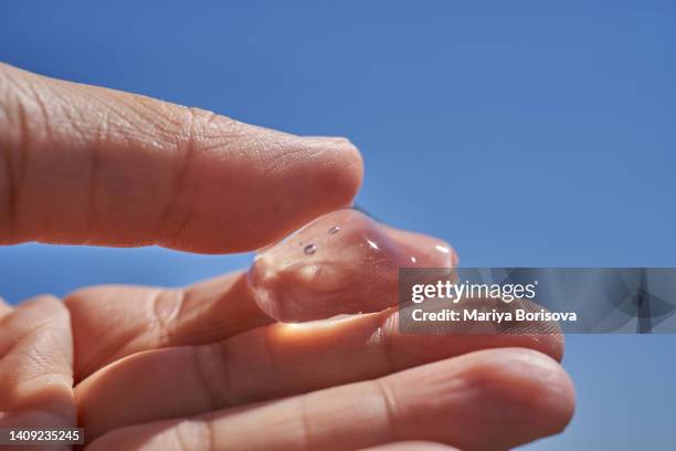 a drop of cosmetic gel on your hand against the sky. the photo can be used as a demonstration of sunscreen or summer products. - gel foto e immagini stock