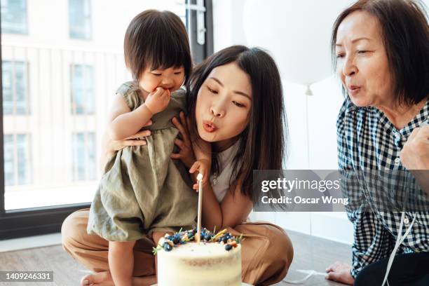 mother and grandmother with baby girl celebrating birthday together - parents children blow candles asians stock pictures, royalty-free photos & images