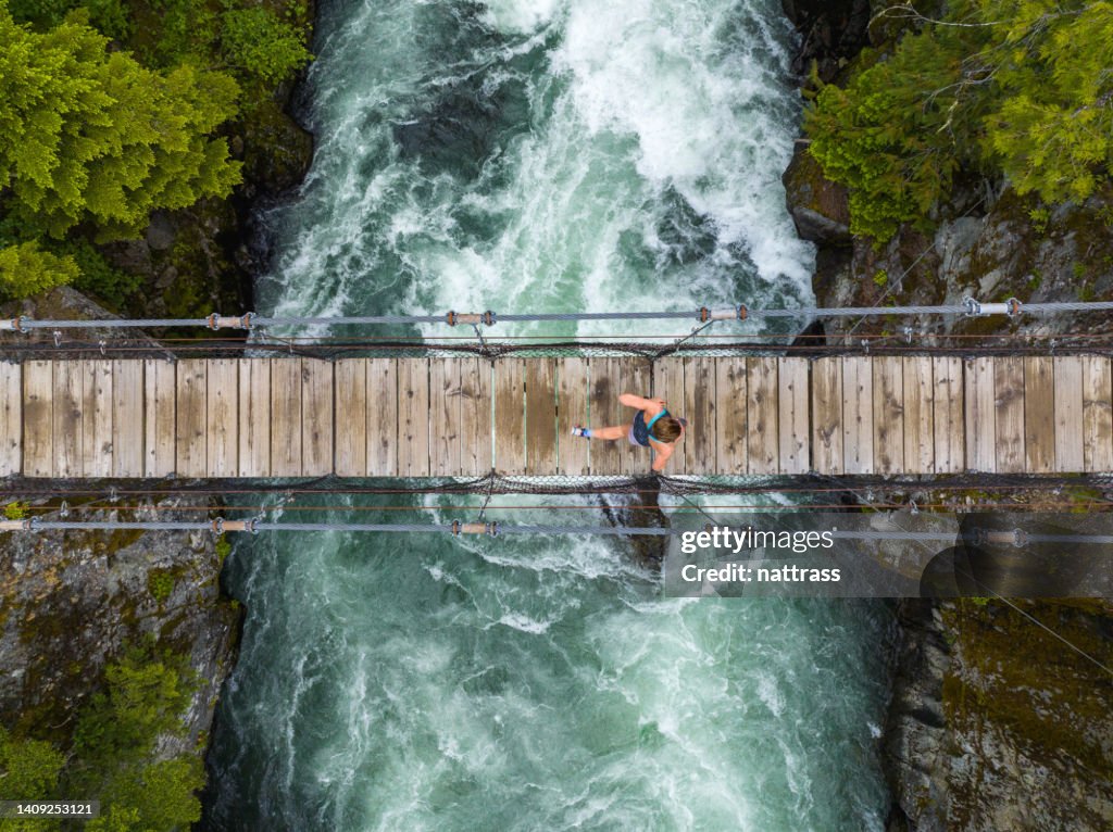 Draufsicht einer Frau, die über eine Hängebrücke über einen Fluss läuft