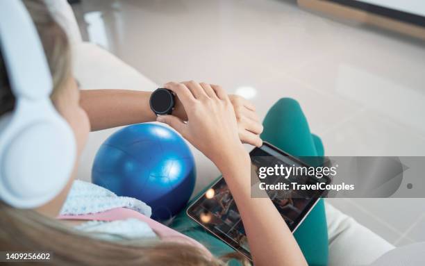 smiling attractive fitness woman with towel after training. fit happy young woman checking applications on smartwatch and smartphone when getting ready to work out at home - time phone stock pictures, royalty-free photos & images