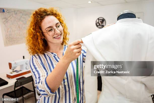 smiling female tailor measuring arm on mannequin pinning needle - mannequin arm stock pictures, royalty-free photos & images