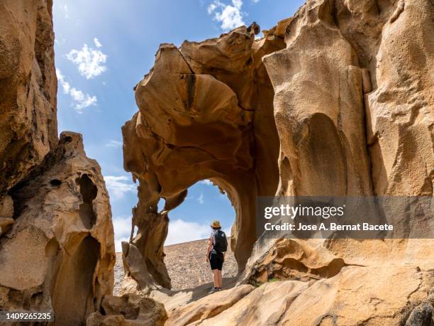 woman sitting resting next to a cave with natural arches produced by erosion on top of a mountain. - fuerteventura stock-fotos und bilder