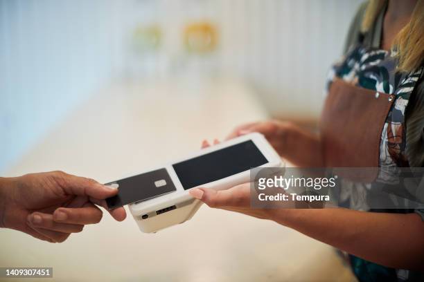 nahaufnahme einer hand, die eine karte auf einem kontaktlosen empfänger hält. - kreditkartenlesegerät stock-fotos und bilder