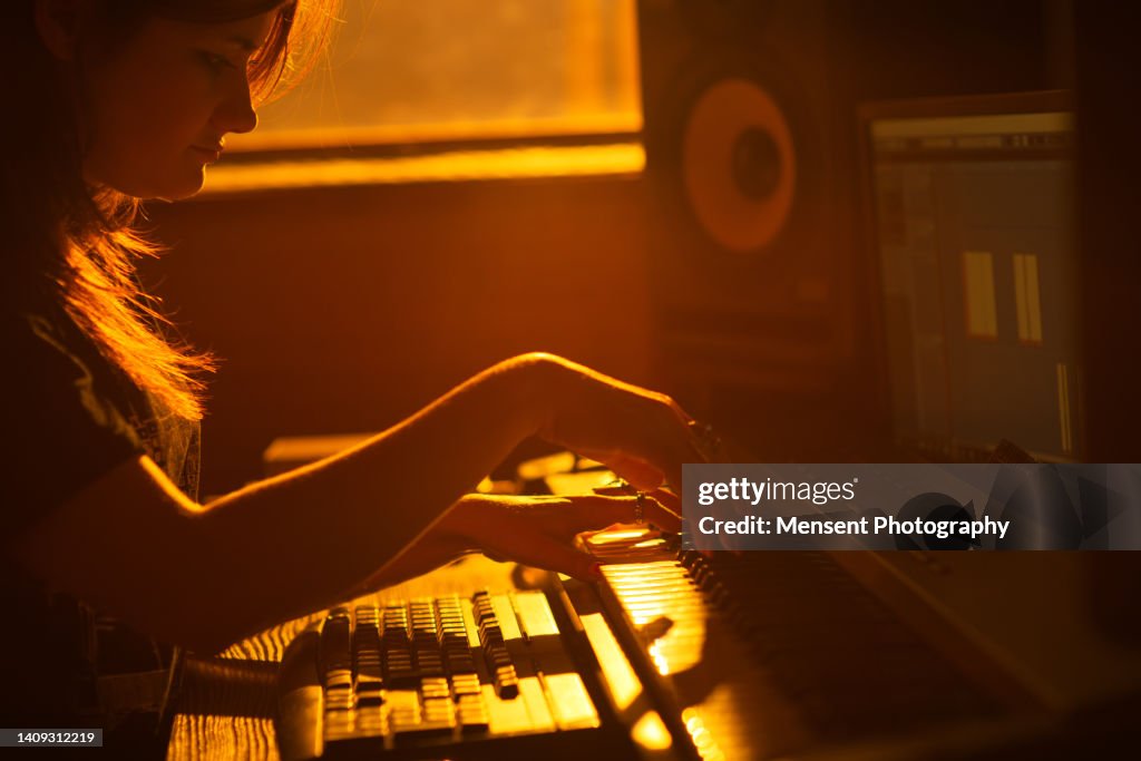 Pianist woman music producer playing piano in professional music recording studio at sunset light close-up